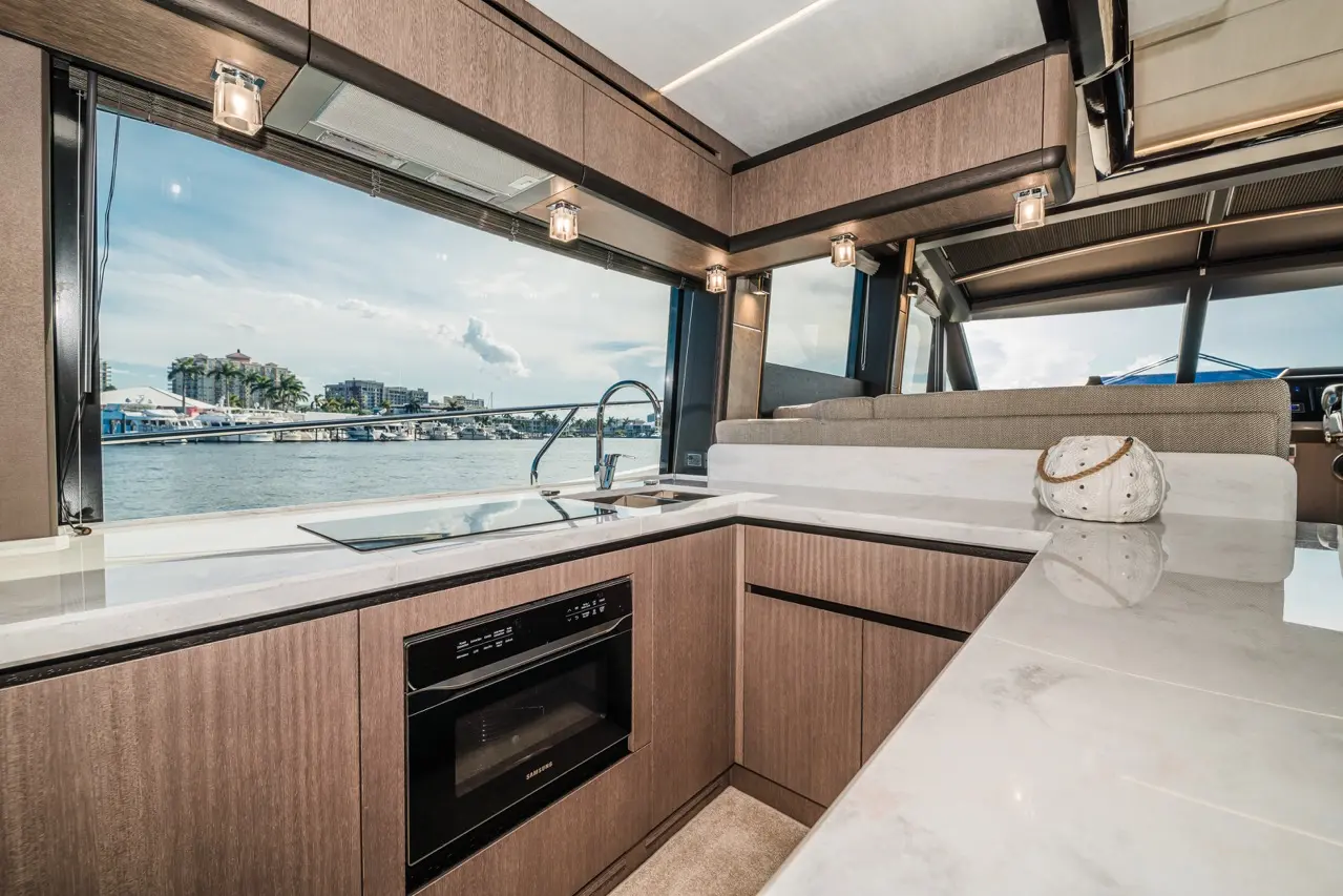 Modern yacht kitchen featuring marble countertops, a microwave, sink with water view, and contemporary wooden cabinetry.