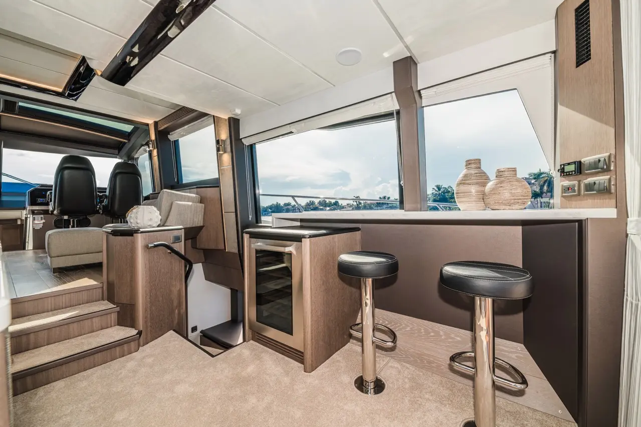 Luxury yacht interior featuring modern seating, a mini bar, and large windows with water view, emphasising spacious elegance.