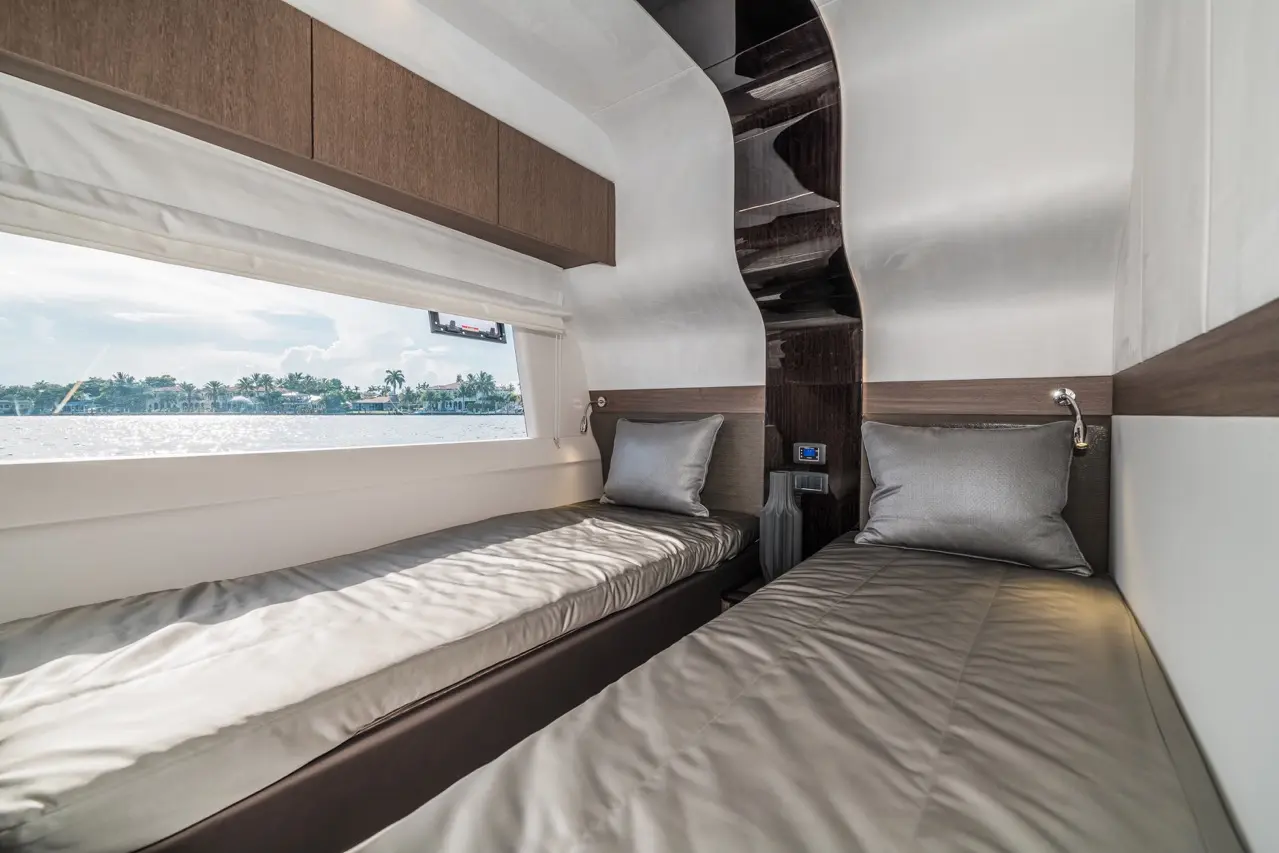 Modern interior of a yacht cabin featuring two single beds, grey cushions, and a large window overlooking water and greenery.