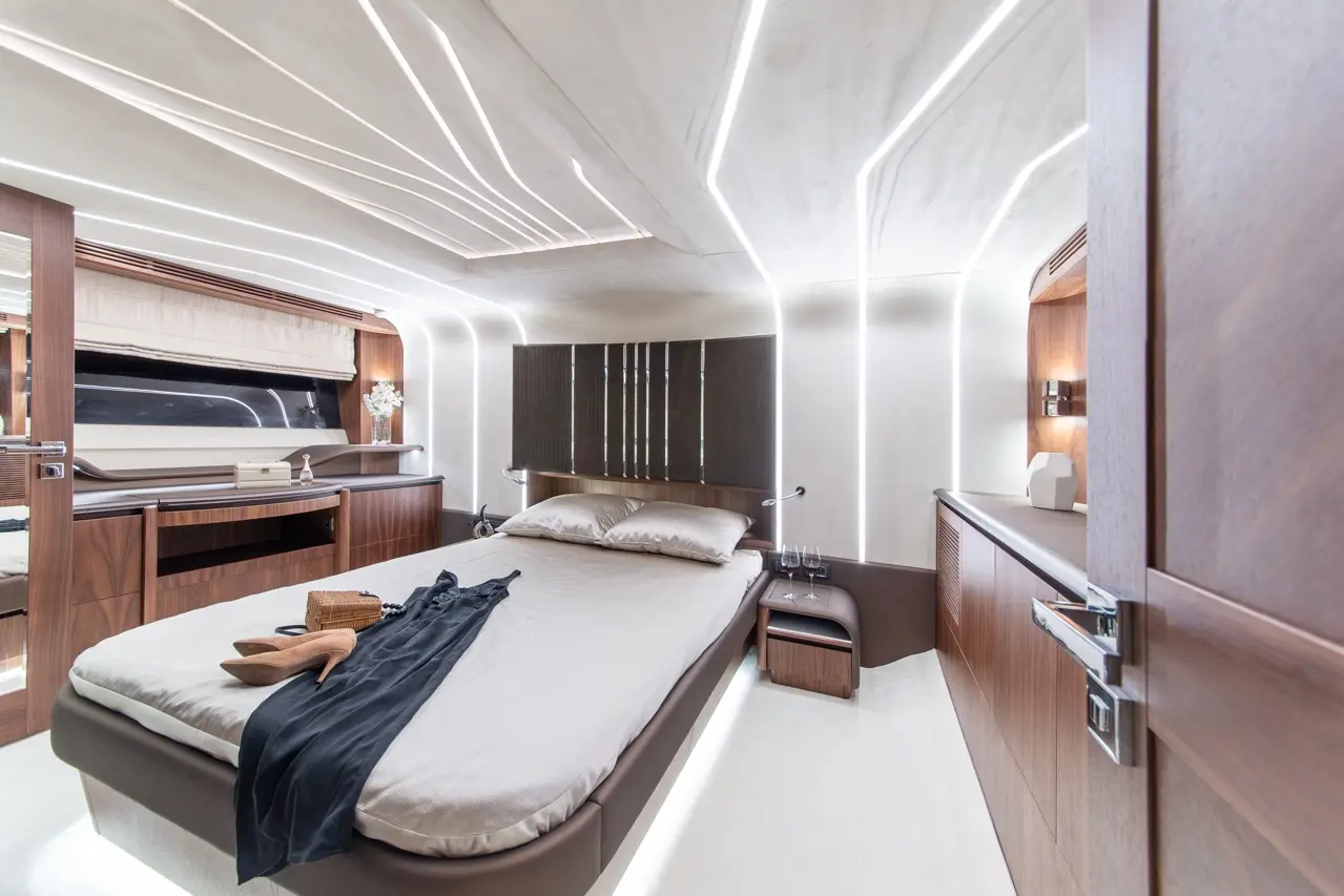 Modern boat interior featuring a double bed, stylish lighting, and wooden cabinetry, with a dress and heels on the bed.