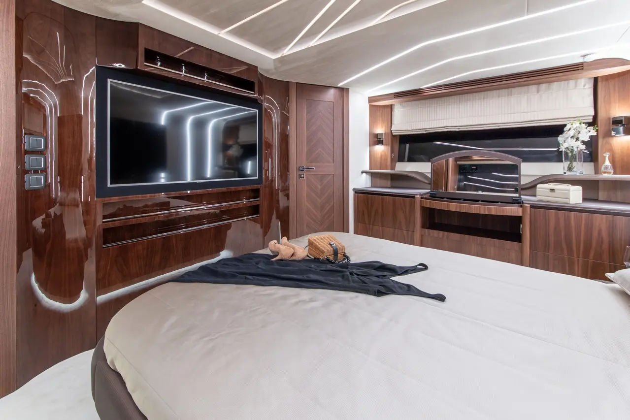 Luxurious yacht bedroom featuring a large TV, elegant wooden furnishings, and a soft bed with a black throw and decorative items.