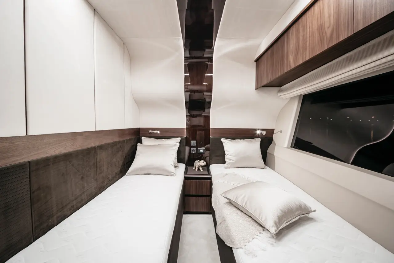 A stylish twin cabin featuring two beds with white mattresses and decorative pillows, contemporary storage, and large windows.