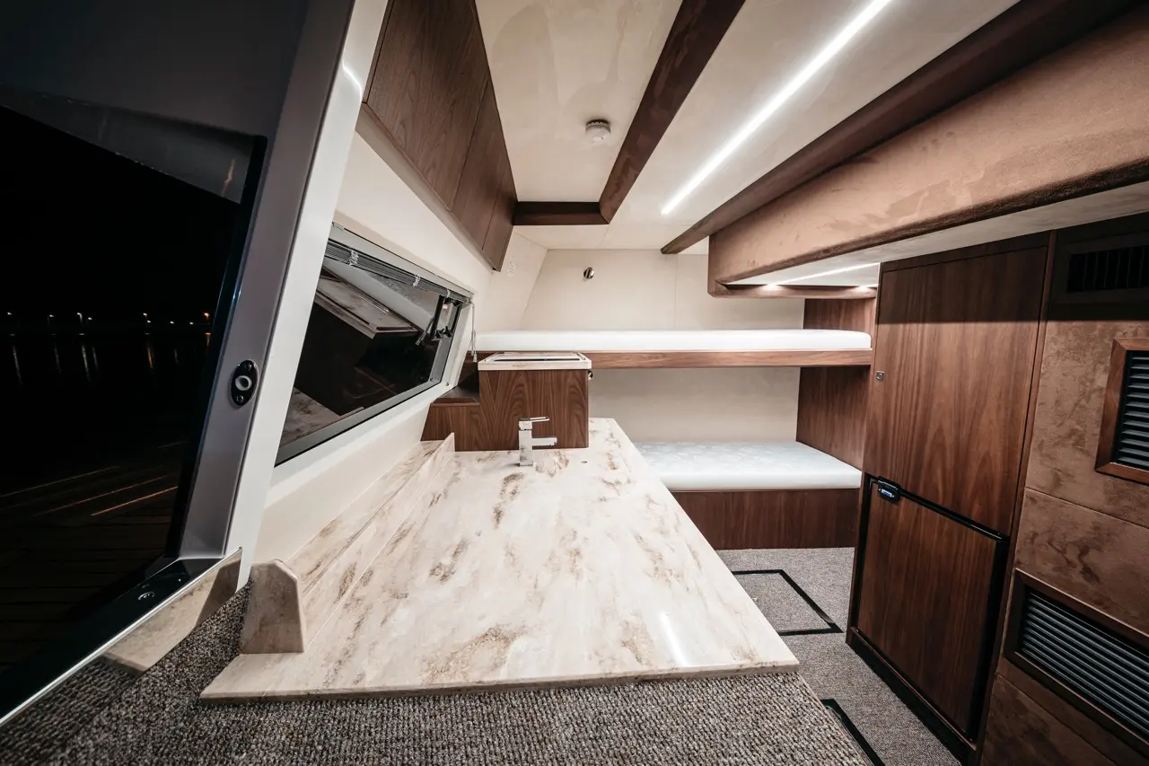 Modern boat interior featuring a marble countertop, wood cabinetry, a sink, and seating area with ambient lighting.
