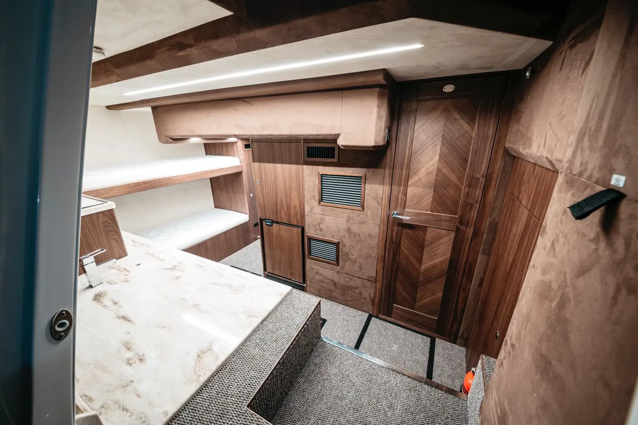 Modern interior of a boat cabin showcasing wooden panelling, a marble countertop, and a staircase leading to a door.