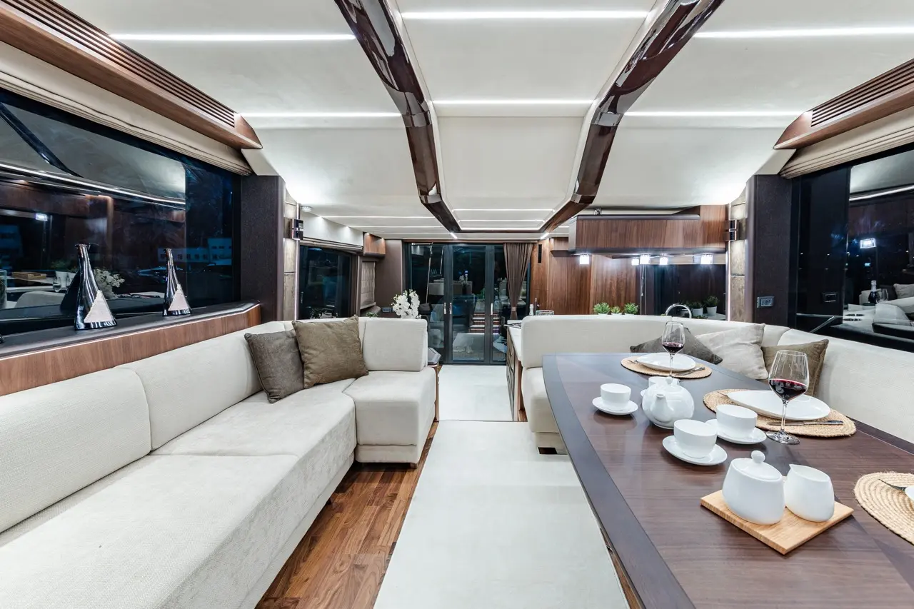 Luxurious interior of a yacht lounge with a dining table, white dinnerware, wine glasses, and plush seating.