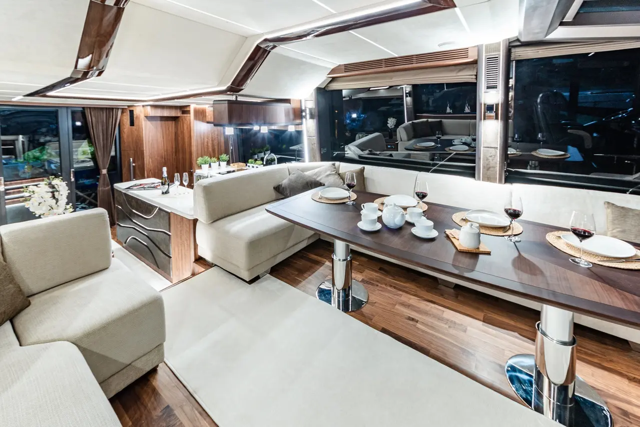 Luxurious yacht interior featuring a dining area with wine glasses, table setting, and modern furnishings. Elegant lighting present.