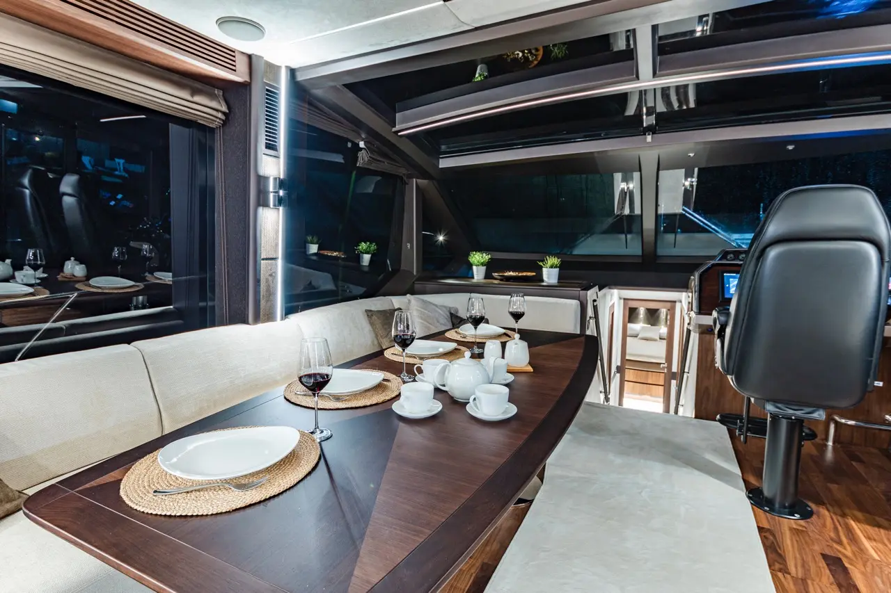 Interior of a luxury yacht featuring a dining table set with plates, glasses, and a helm chair, lit by soft ambient lighting.