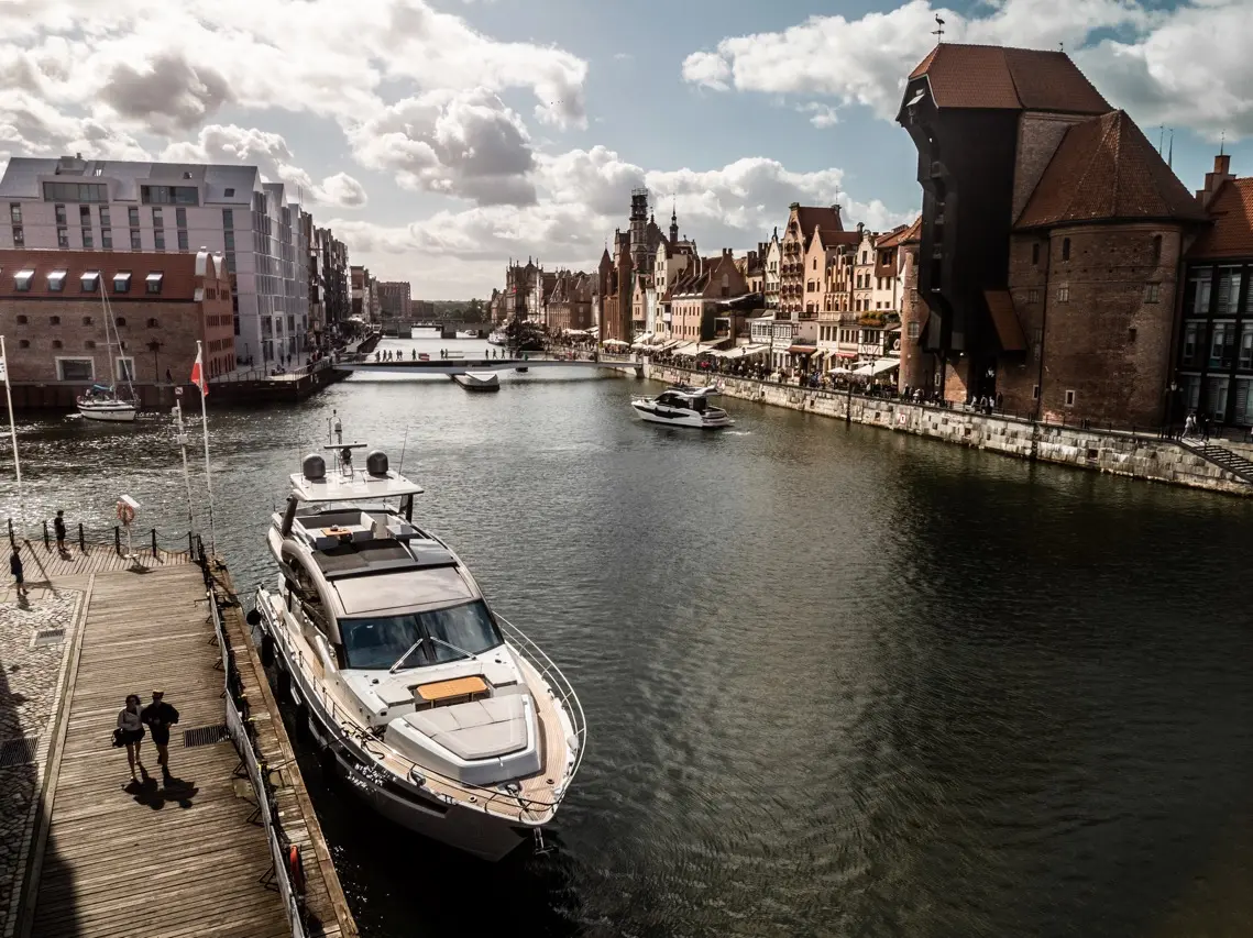 Scenic waterfront in Gdańsk with yachts and people walking along the promenade by beautiful historical buildings.