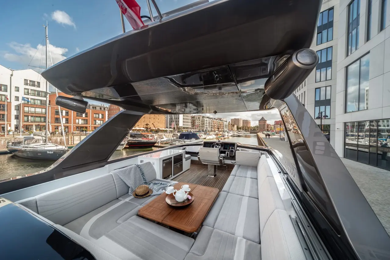 Luxury yacht interior with seating and a dining table, overlooking a marina filled with boats and modern buildings.
