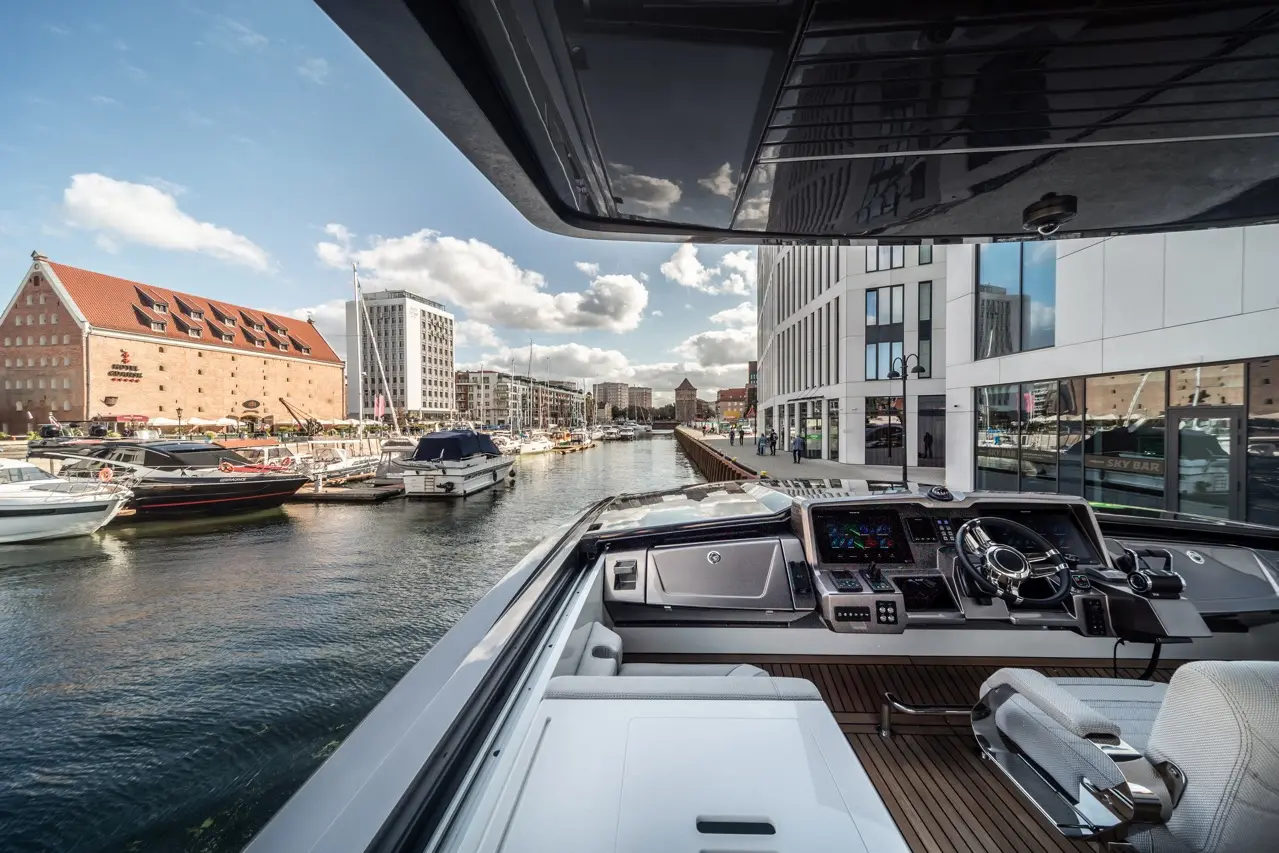 View from a modern yacht, featuring the control dashboard, boats in the marina, and contemporary buildings along the water.