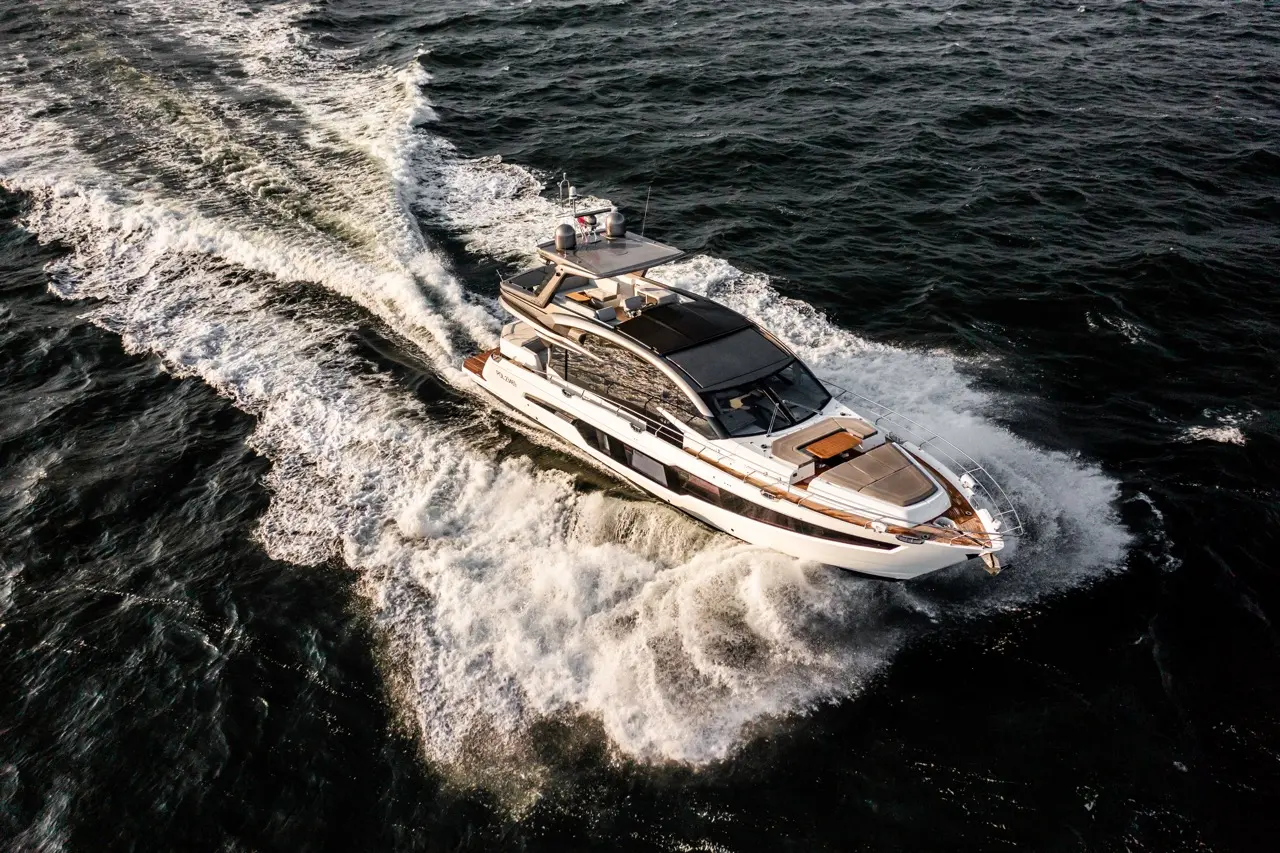 Luxury yacht cruising through choppy waters, creating white frothy waves at its stern on a sunny day.