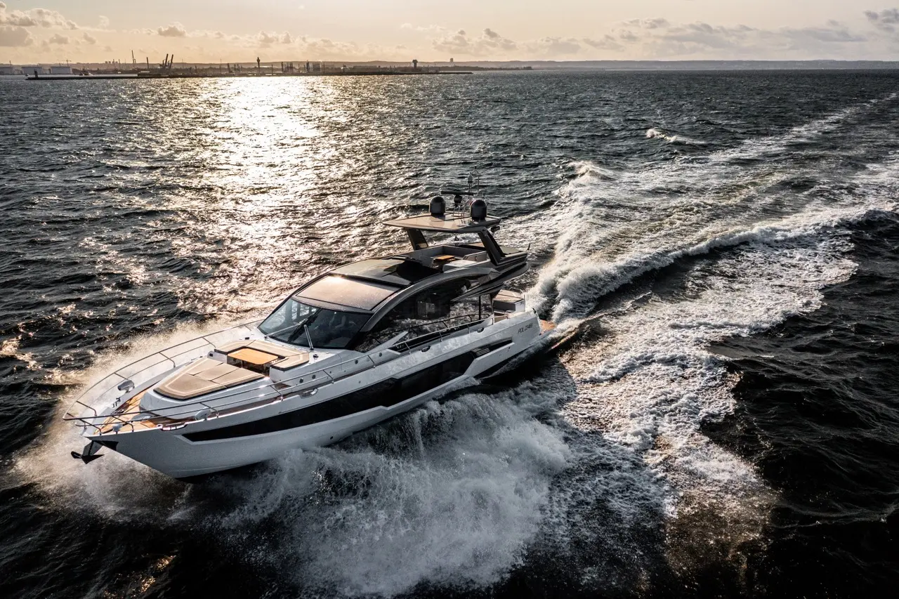 Luxury motor yacht navigating through sparkling ocean waters during sunset, with a city skyline in the background.