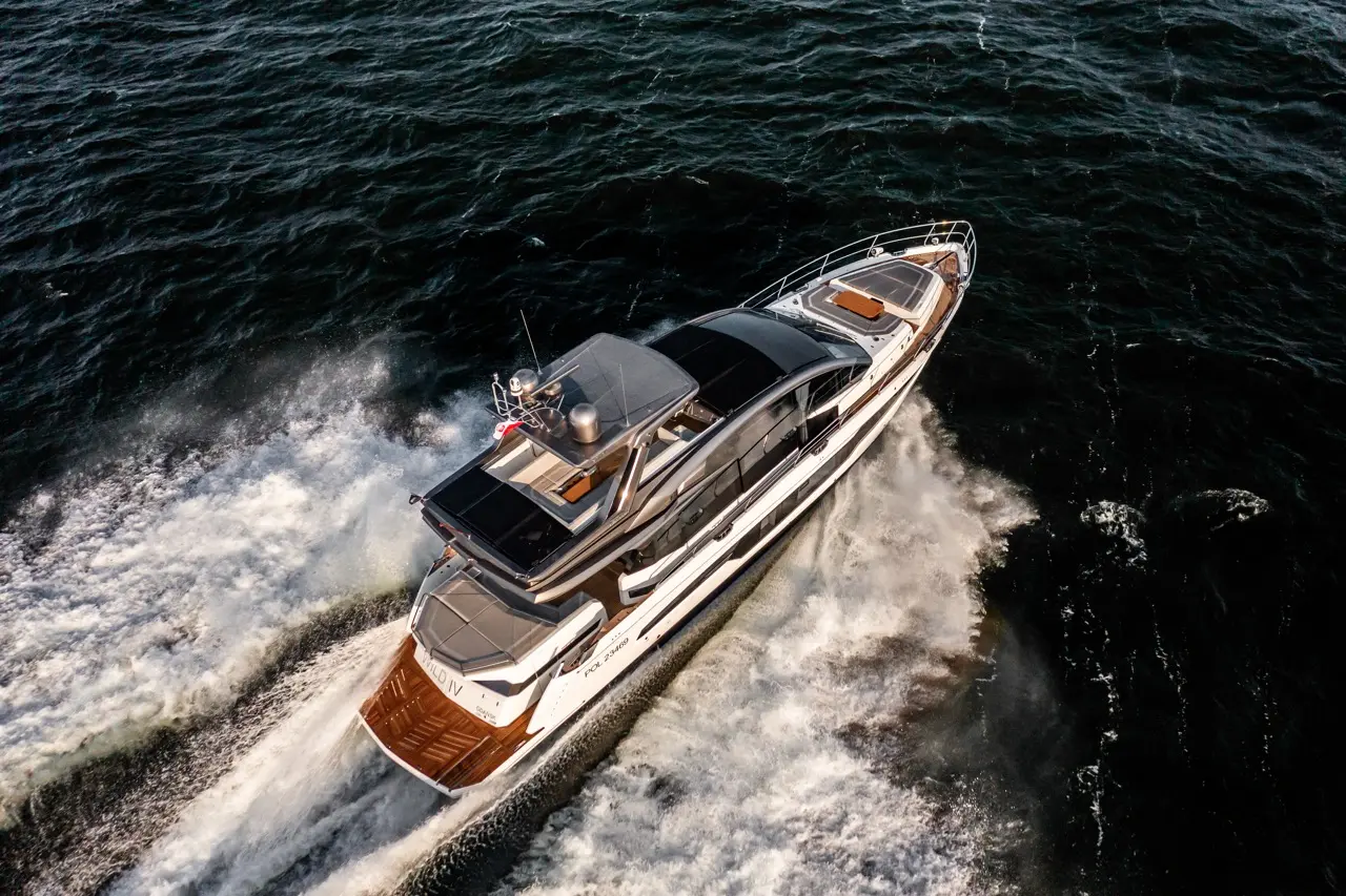 Luxury motor yacht cruising through dark waters, creating a wake with sunlight reflecting off the surface.