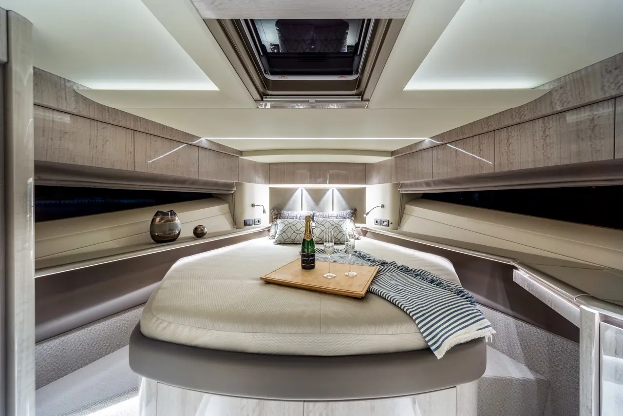 Luxurious boat interior with a round bed, champagne, and glasses on a tray, featuring soft lighting and sleek wood cabinetry.