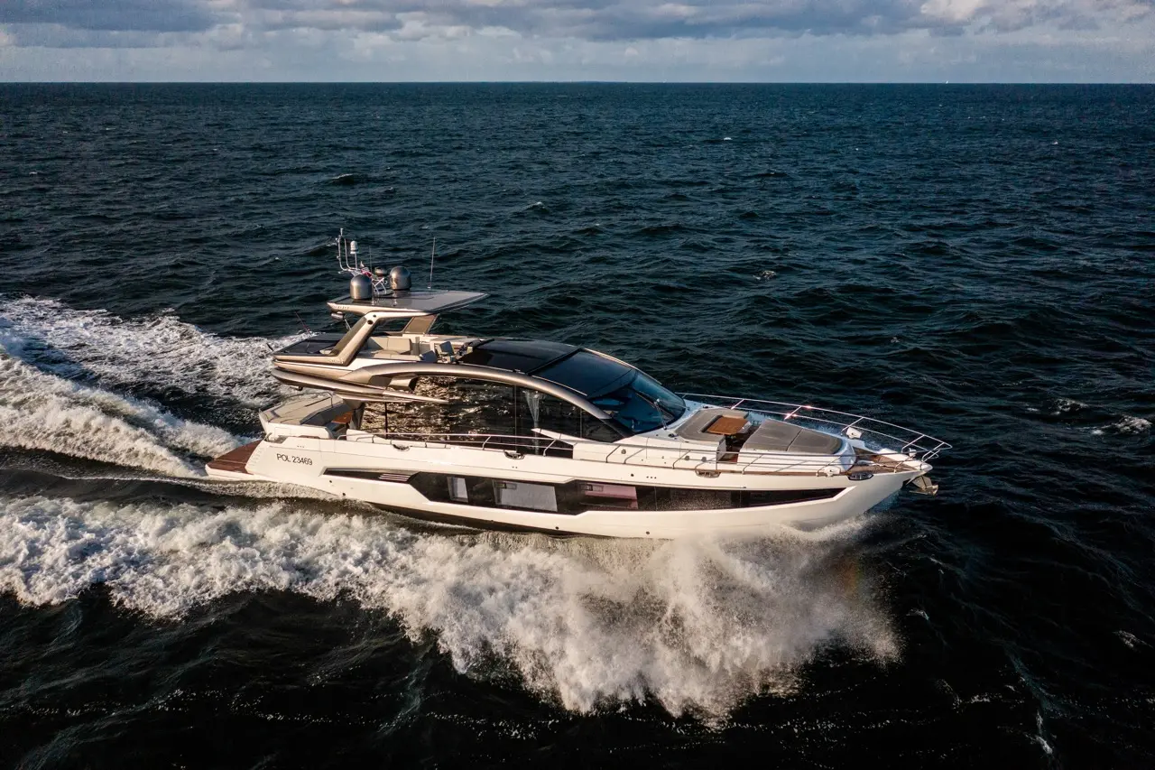 A luxury yacht cruising through ocean waves, leaving a frothy wake under a partly cloudy sky.