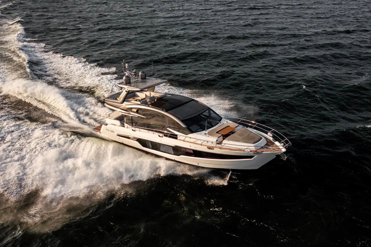 A luxury yacht glides through the water, leaving frothy waves behind against a dark ocean backdrop.