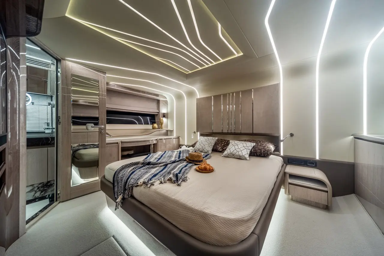 Modern bedroom with elegant lighting, a large bed, decorative cushions, and a small table with pastries and a hat.
