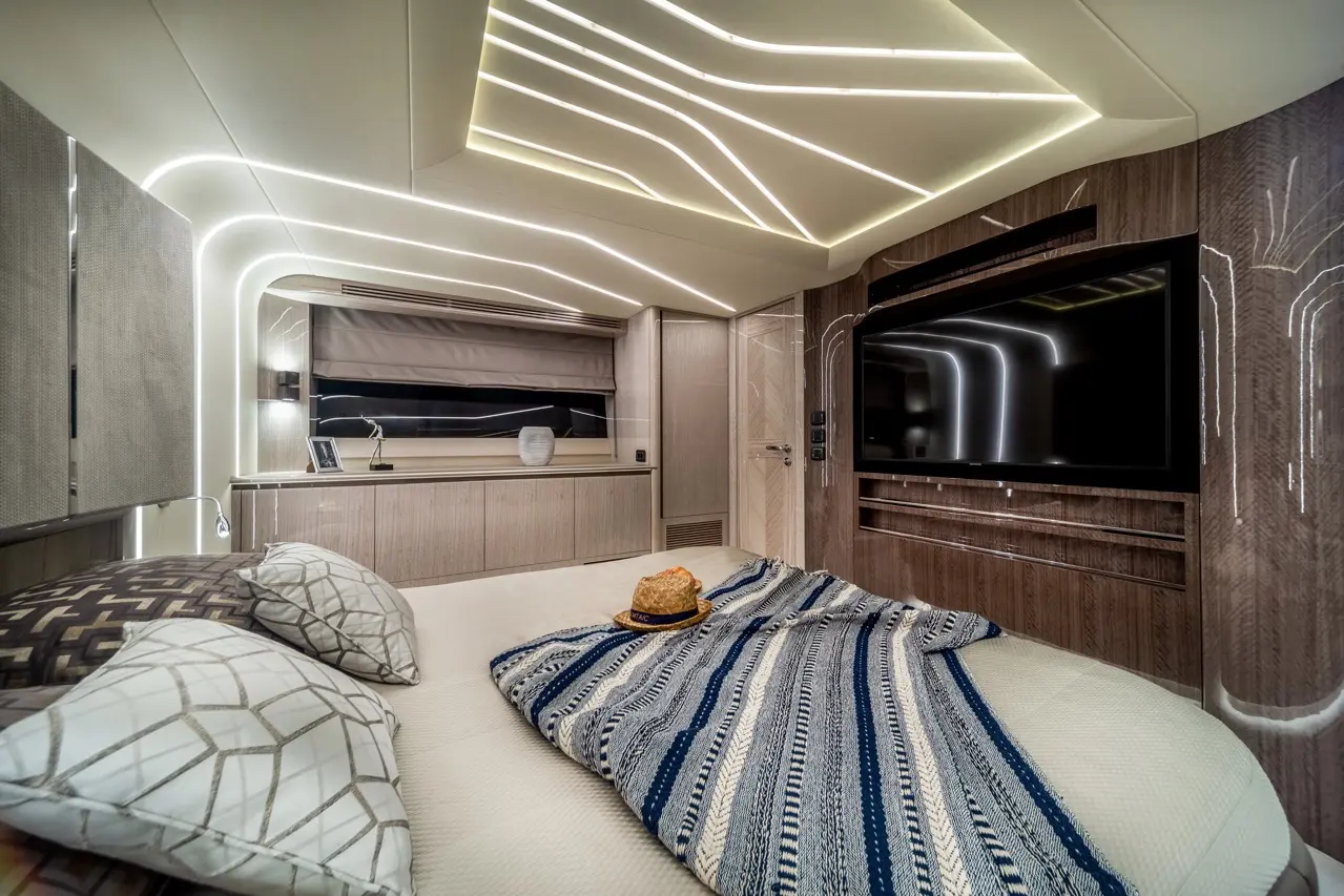 Modern bedroom with sleek design, ambient lighting, a patterned blanket, decorative pillows, and a TV unit.