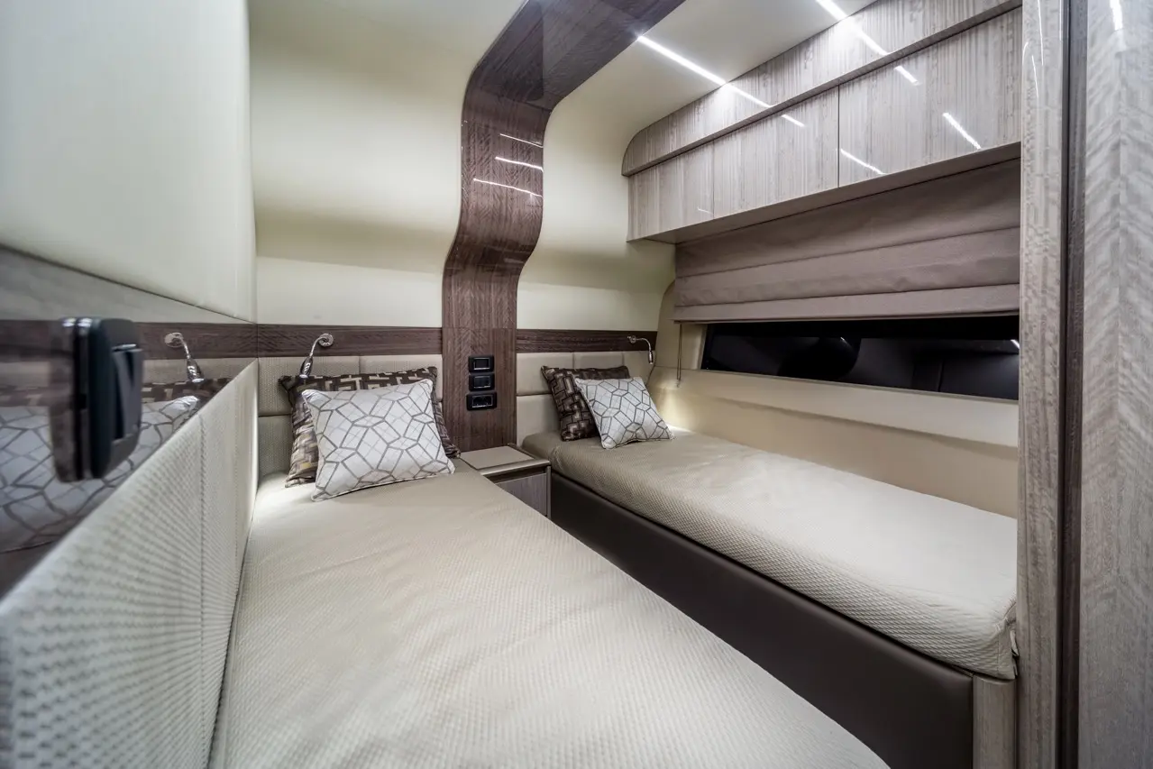 Modern cabin with two single beds, cushions, stylish wooden accents, overhead storage, and ambient lighting.