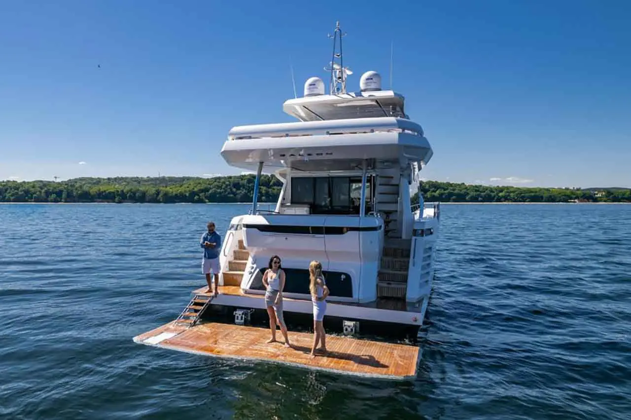 People enjoying a luxury yacht on the water, with one man standing and two women on the boarding platform.