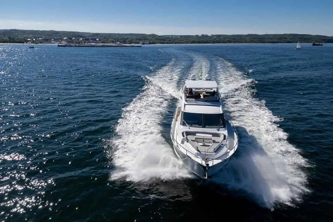 A sleek motorboat speeds through shimmering waters, creating waves against a scenic coastal backdrop.