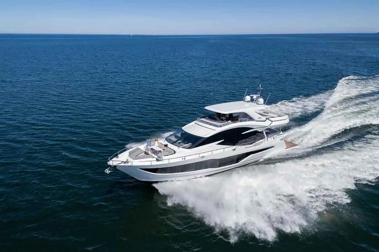 A sleek white yacht gliding through calm blue waters, leaving a foamy wake and enjoying sunny weather.