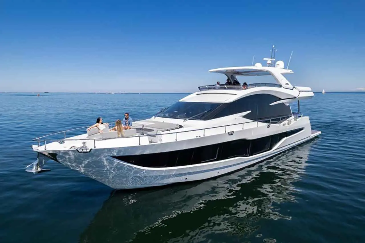 A luxurious white yacht anchored on calm waters, with three people relaxing on the deck under a clear blue sky.