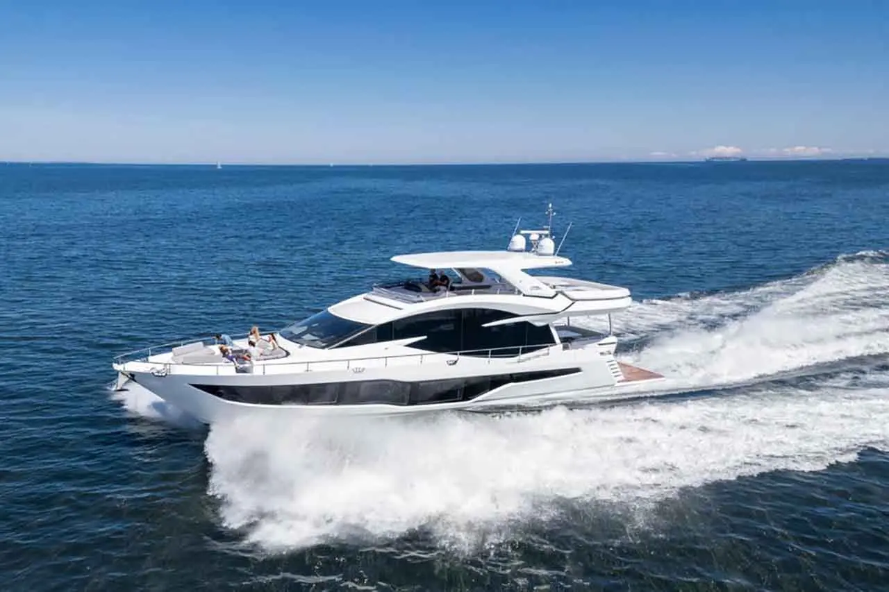 Luxury motor yacht cruising over calm waters, creating a wake with passengers relaxing on the upper deck under clear blue skies.