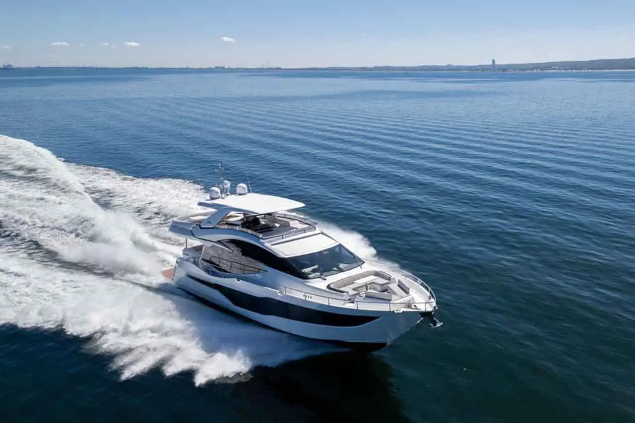 A luxury motor yacht speeds across calm blue waters, leaving a wake under a clear sky with scattered clouds.