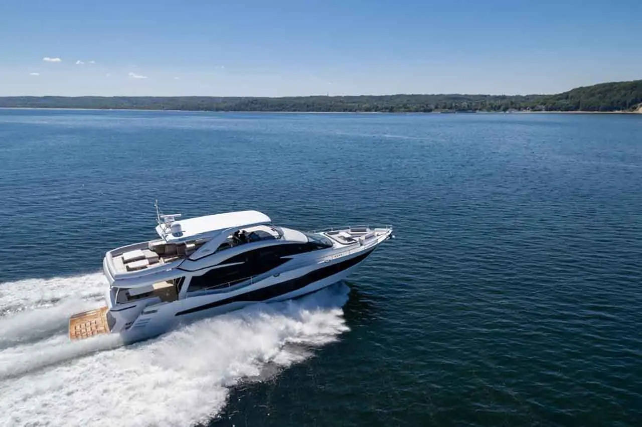 A luxury yacht navigates through calm waters under a clear blue sky, leaving a white wake behind it.