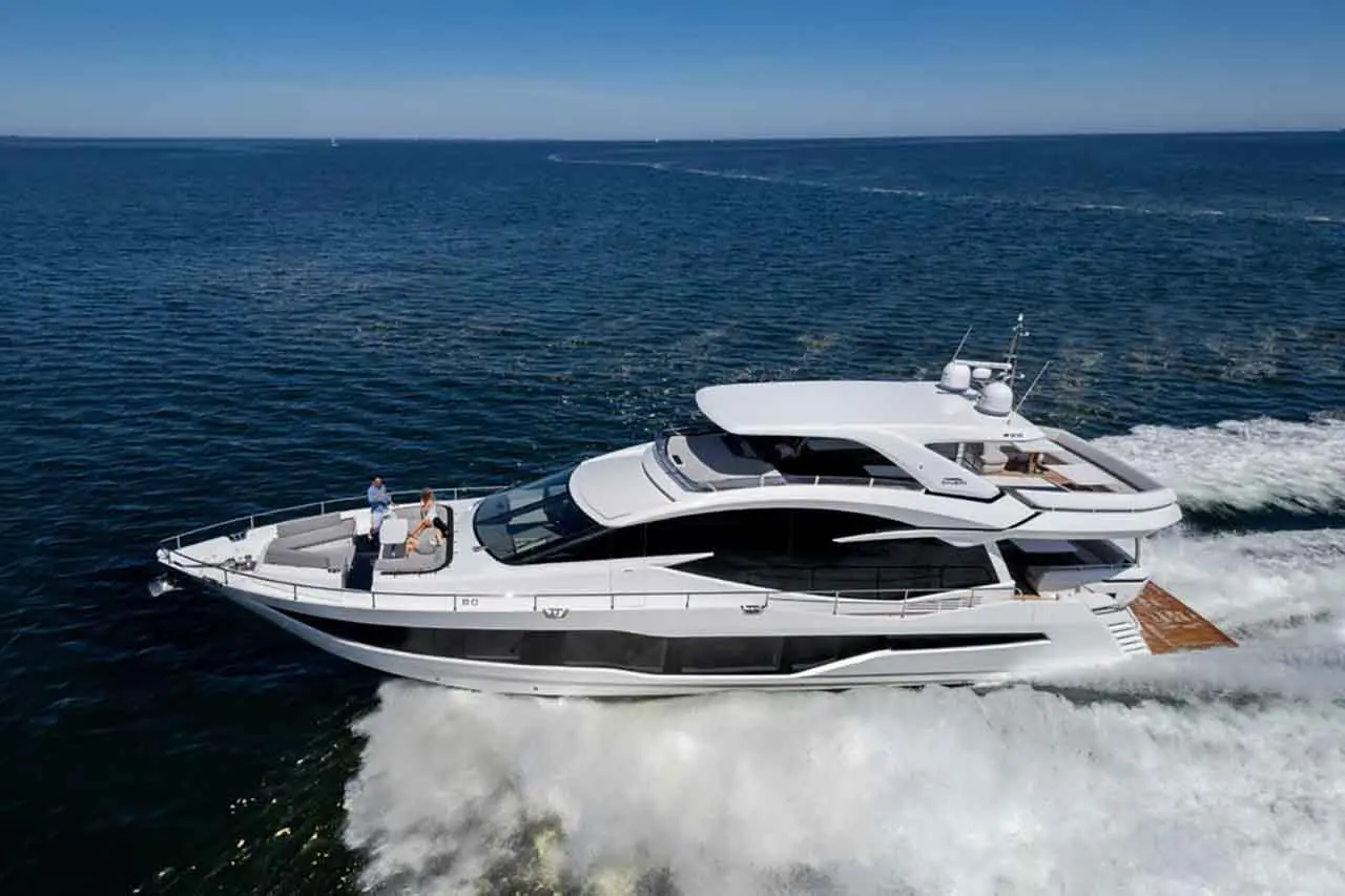 A luxury motor yacht cruising through the ocean, with two people on board enjoying the sea view.