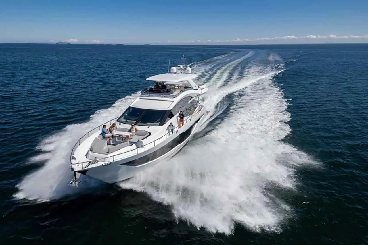 A luxury yacht speeds across the ocean, leaving a spray of water, with people enjoying the sun on the deck.
