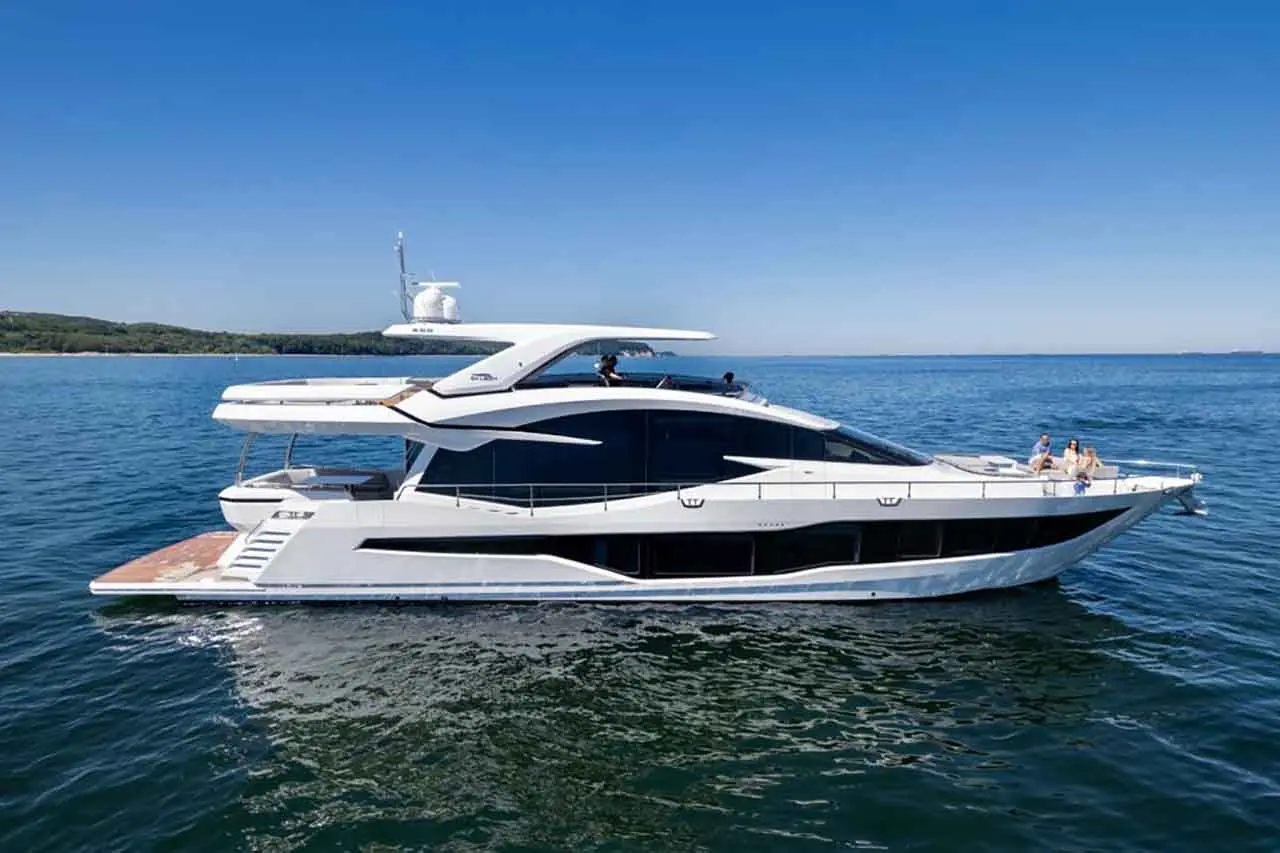 Luxury yacht sailing on calm waters, with people relaxing on deck under a clear blue sky.