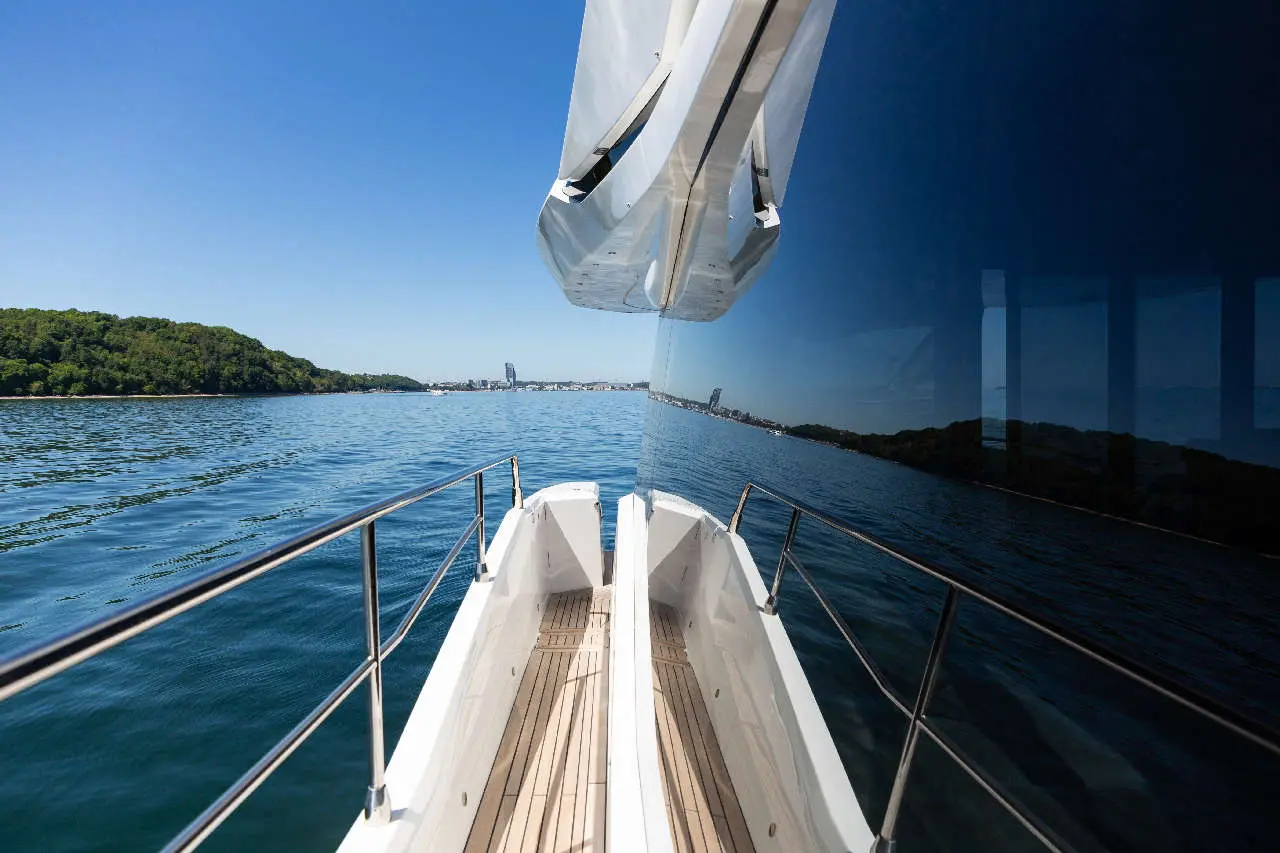View from the bow of a luxurious boat, reflecting clear water, trees, and a city skyline under a bright blue sky.
