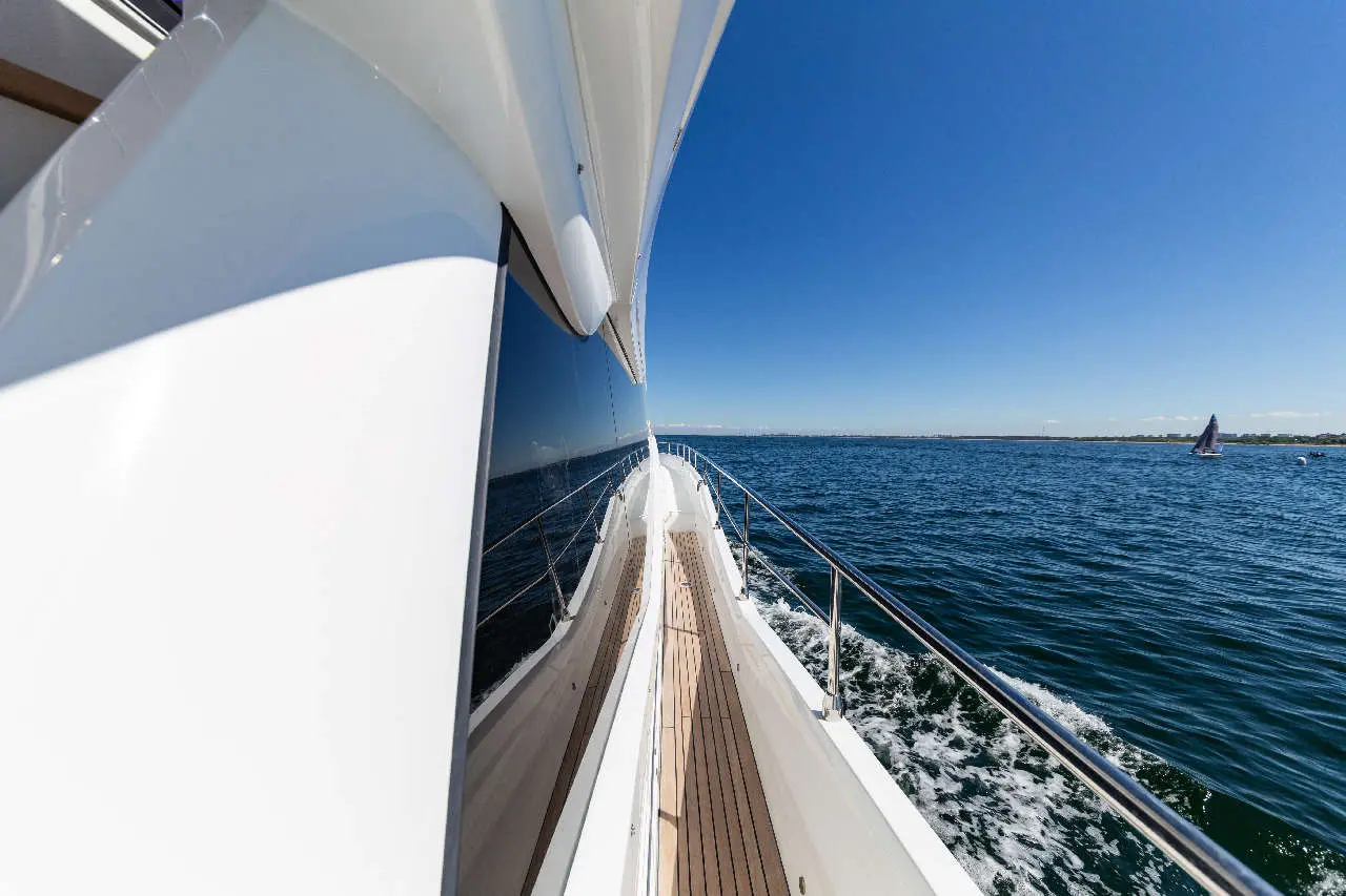 View from a yacht's deck, showcasing clear blue water, sunny sky, and a distant sailboat in the background.