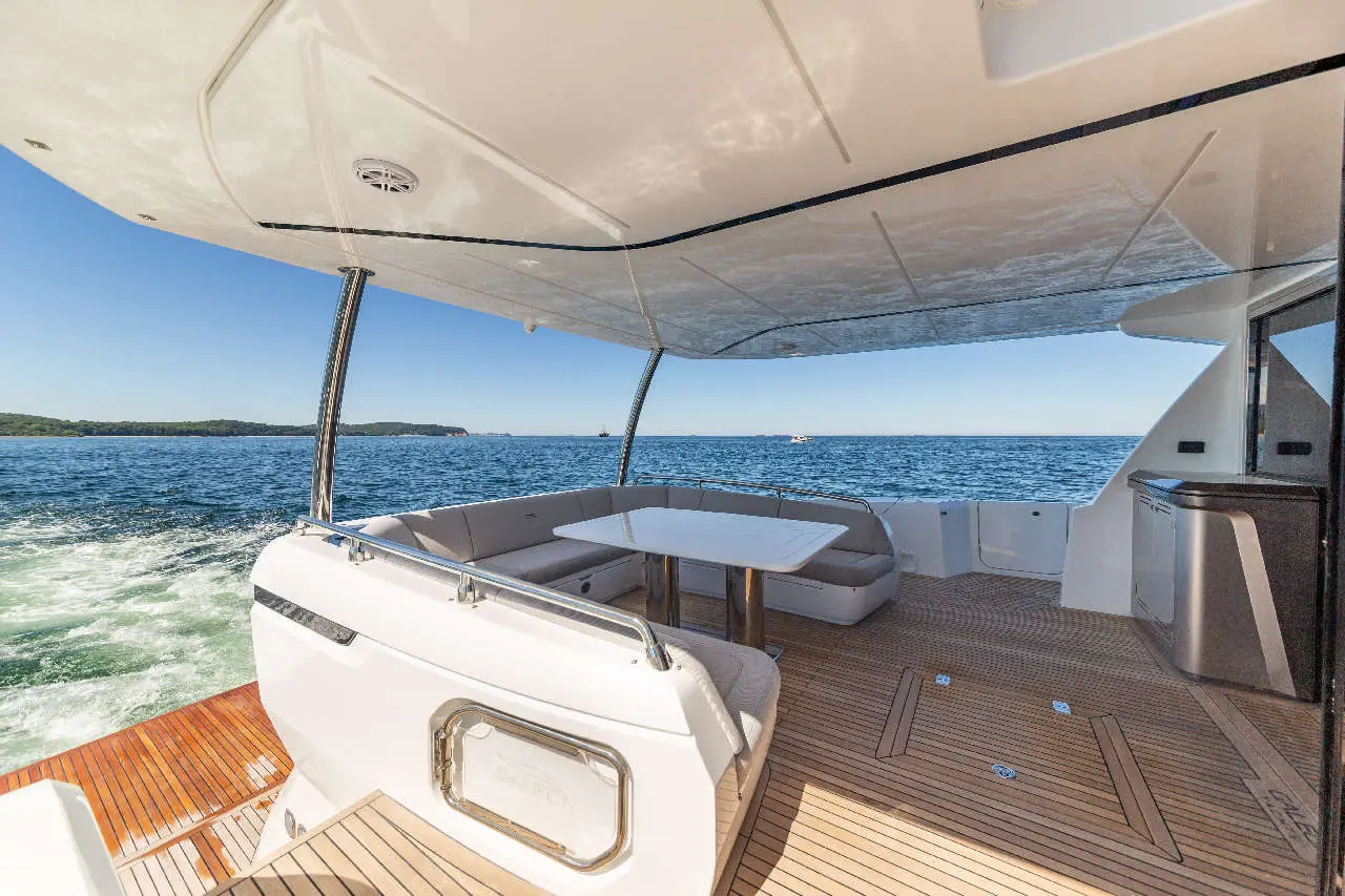 Luxury yacht interior featuring a dining area, plush seating, and panoramic sea views on a sunny day.