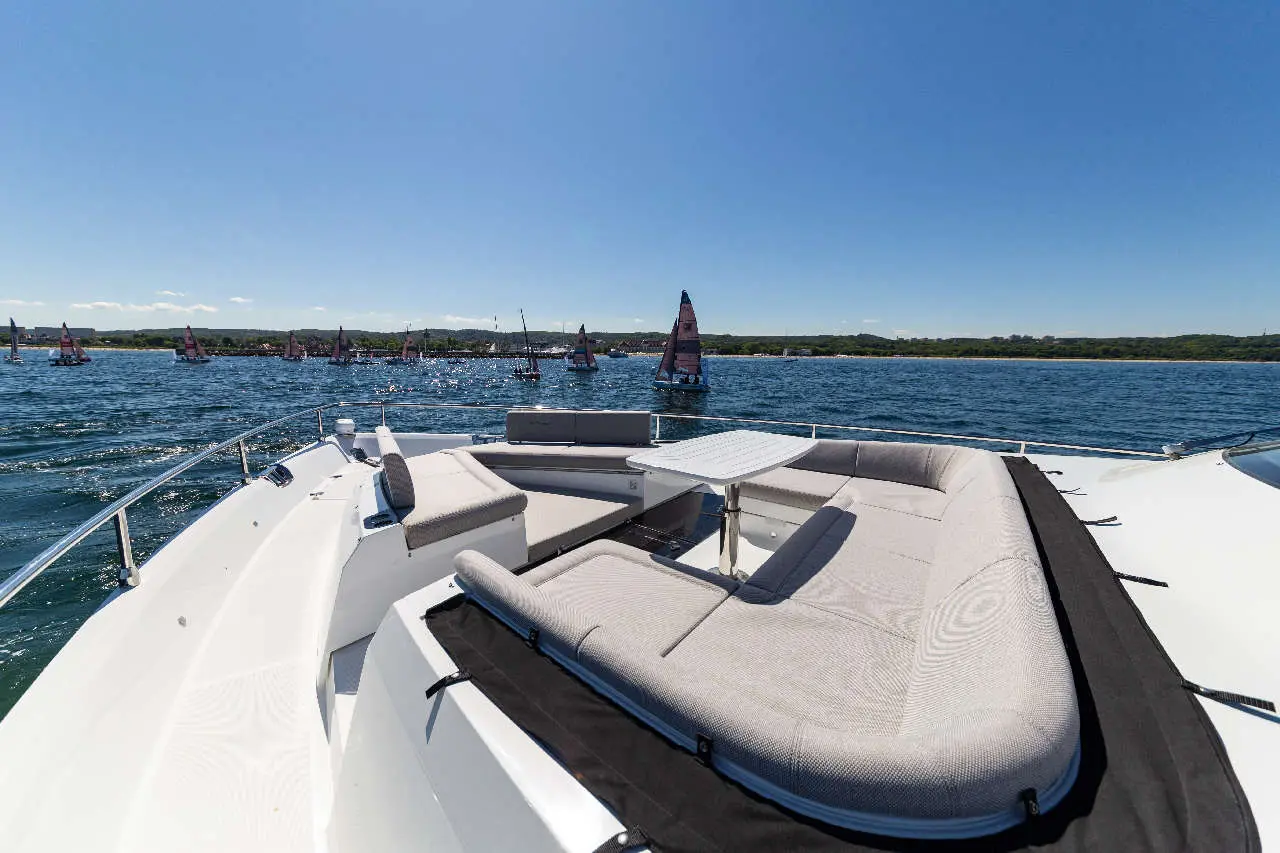 A spacious boat seating area overlooks a bay with several sailboats in the distance under a clear blue sky.