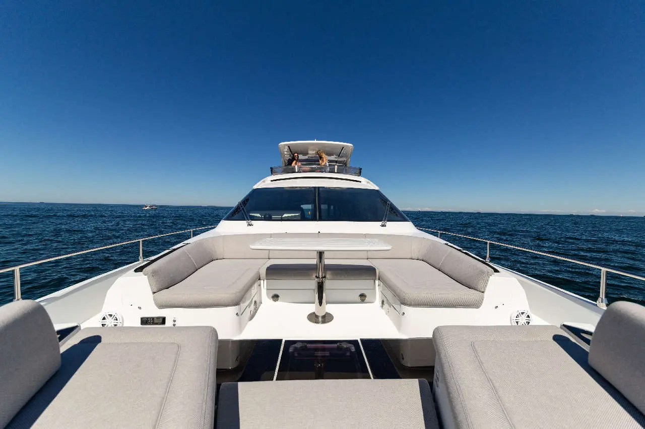 Luxury motorboat’s deck with grey cushions, featuring seating and a table, overlooking a calm sea under a clear blue sky.