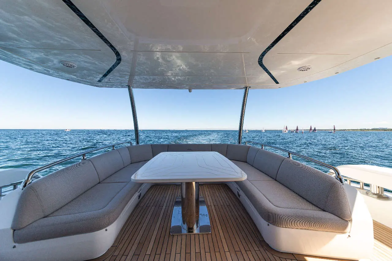 View from inside a boat showing a cosy seating area with a table, overlooking the water and sailboats in the distance.
