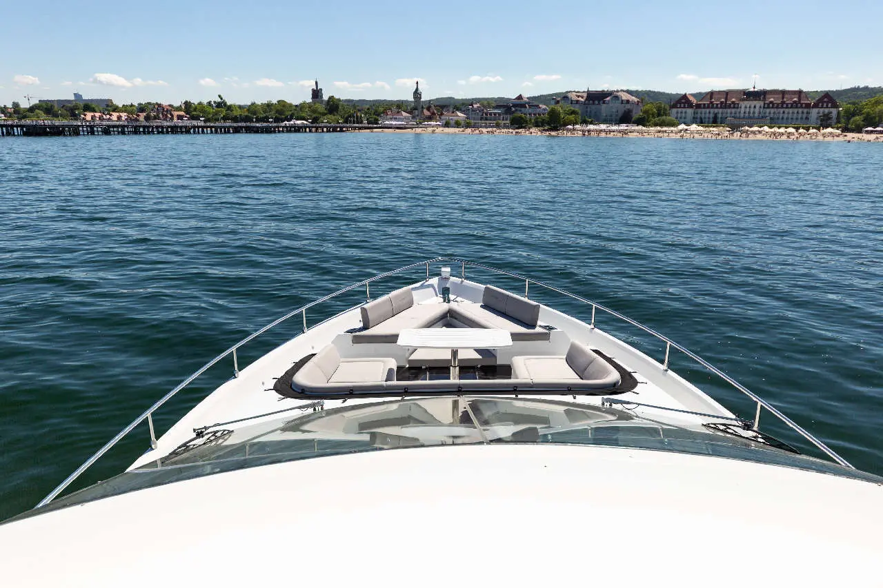 Bow view of a luxury boat on calm water, showcasing comfortable seating and a distant shoreline under a clear blue sky.