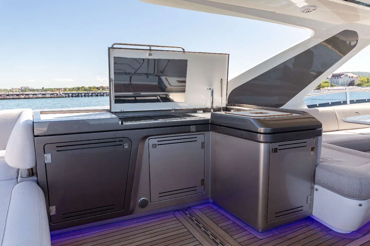 Modern boat kitchenette with a grill and sink, blue ambient lighting, and water views in the background.
