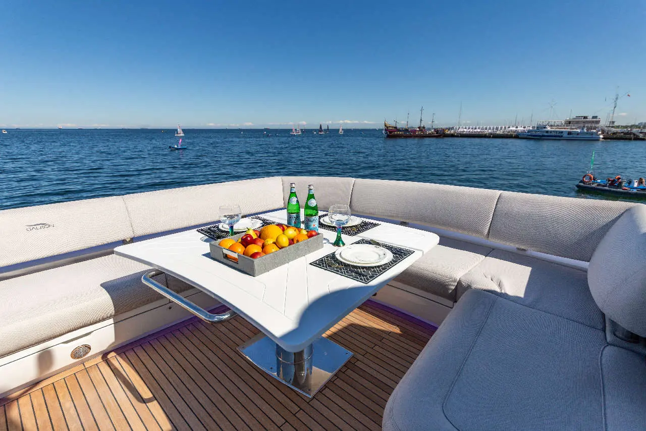 Luxe yacht setting with a white table, fruit platter, drinks, and scenic sea view, perfect for relaxation and dining.