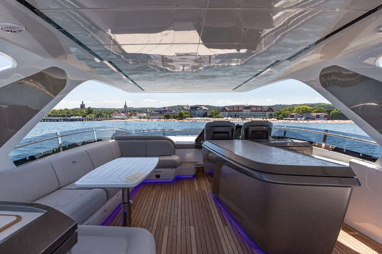 Luxury yacht interior with grey seating, table, and scenic view of a beach town across the water.