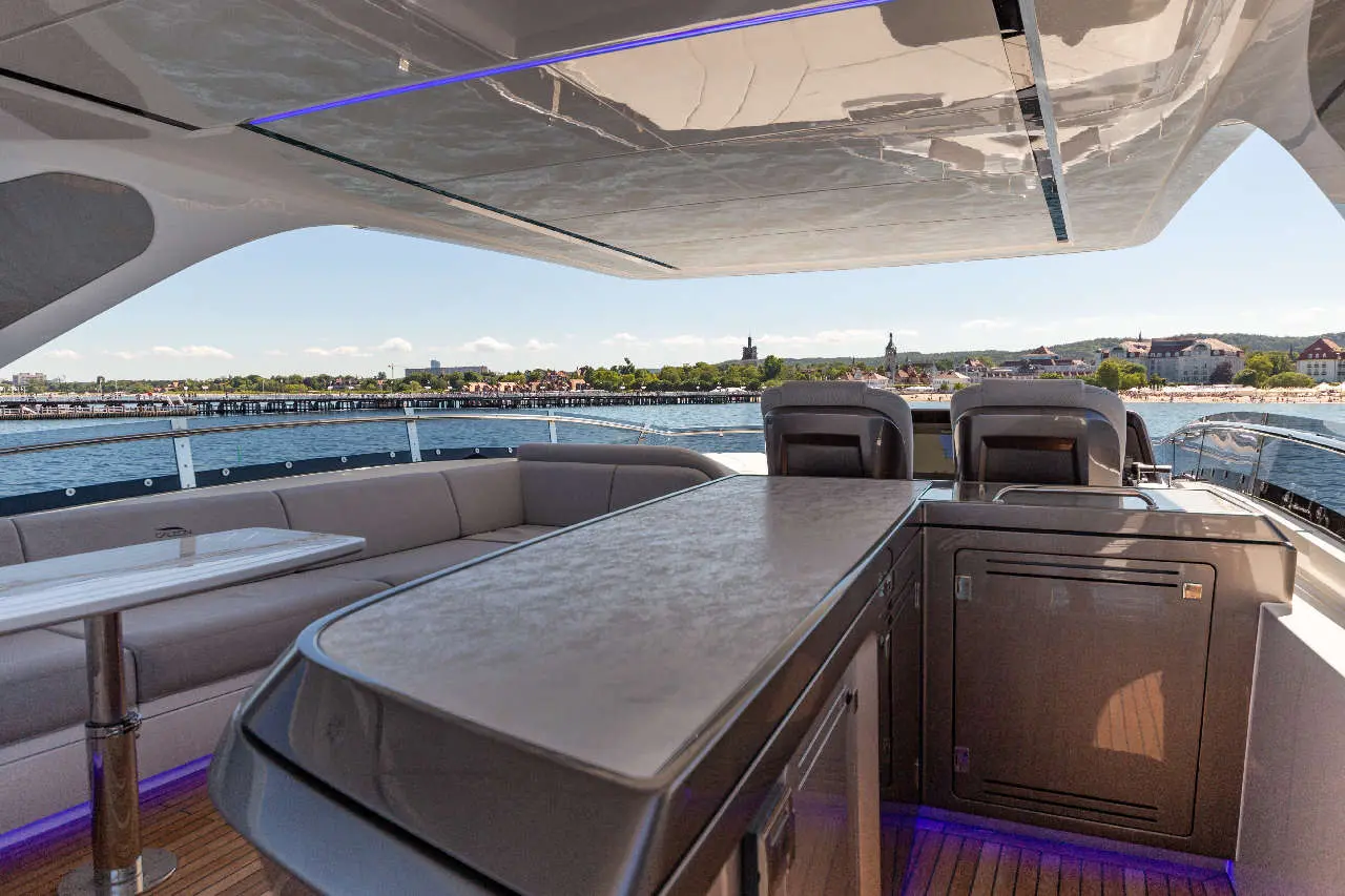 Luxury yacht interior with a seating area and a bar, overlooking a marina with buildings and greenery in the background.