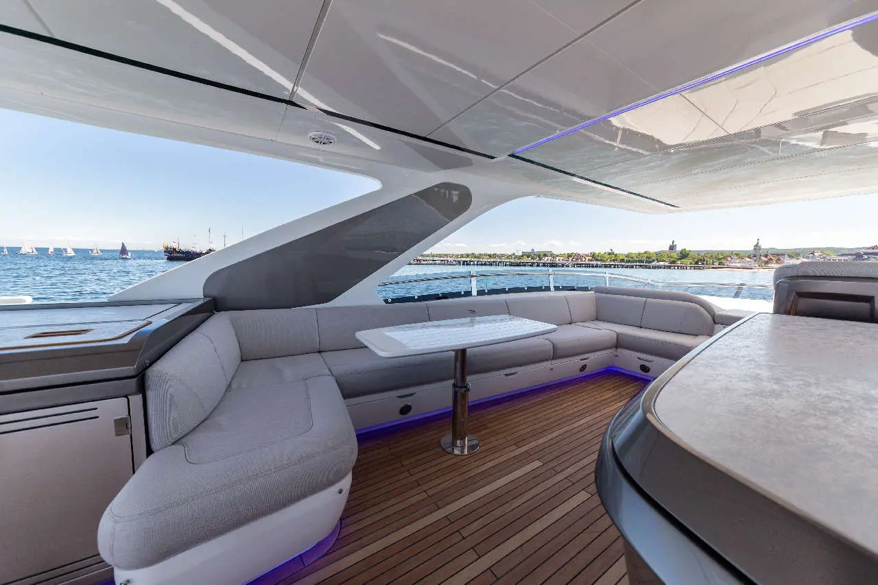 Luxury yacht interior featuring grey seating, a dining table, and a view of moored sailboats on the water.