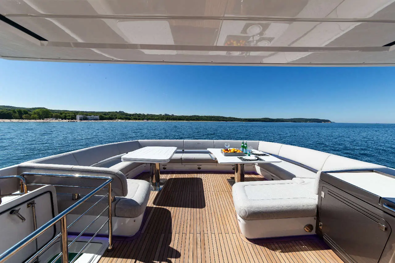 Luxury yacht deck with seating, table set with snacks and drinks, offering a view of calm blue waters and greenery.