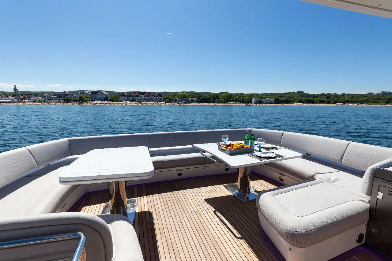 Luxury yacht deck with seating, a table set with drinks and fruit, and a scenic water view under a clear blue sky.