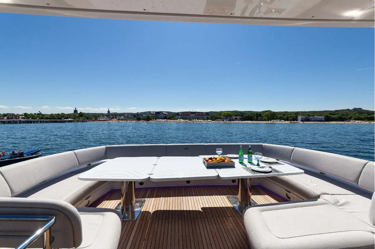 Luxury yacht interior with a dining area, sparkling water view, fruits, drinks, and blue sky in the background.