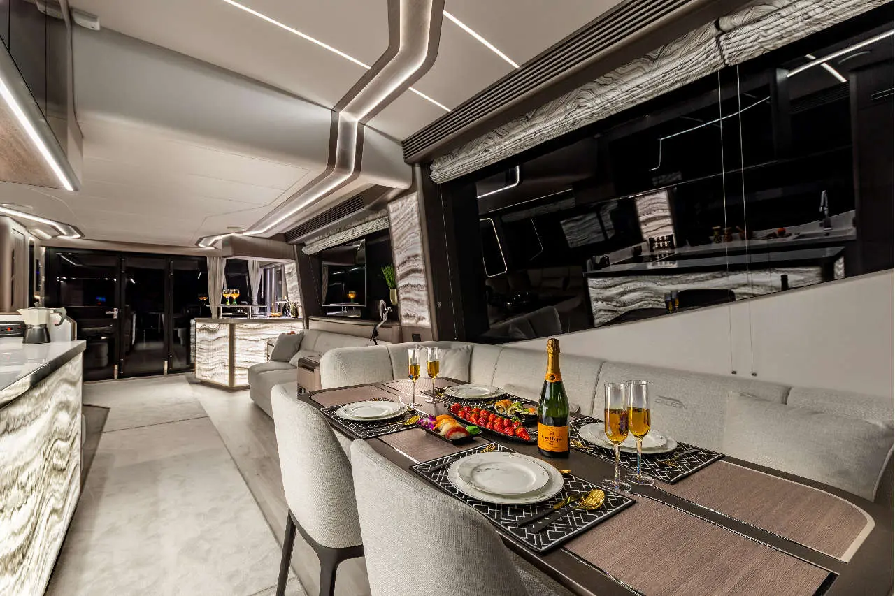 Luxurious yacht dining area with elegant table set, champagne, fresh fruit, and modern decor against a dark backdrop.