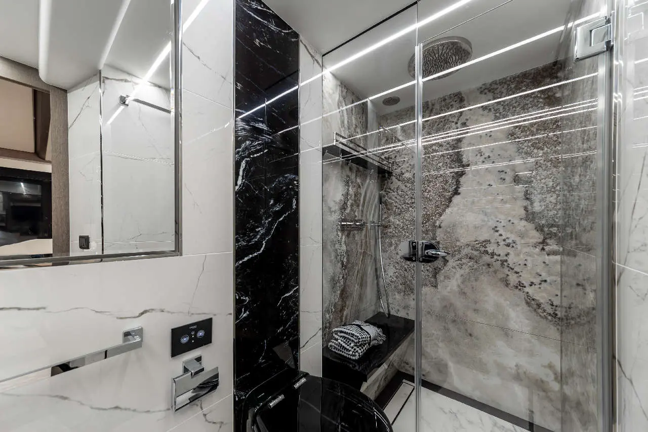 Modern bathroom featuring sleek black and white marble, glass shower, and a towel on a black bench. Minimalist design.